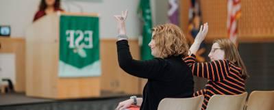 Two people seated with raised hands in an auditorium.